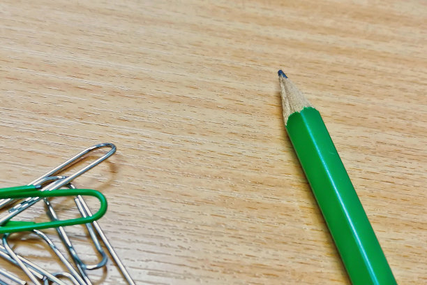 近距离的绿色铅笔在棕色的木头表面背景与回形针。图片下载