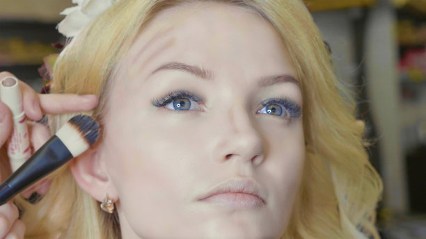 年轻的化妆师在模特脸上涂抹遮瑕膏。图片下载