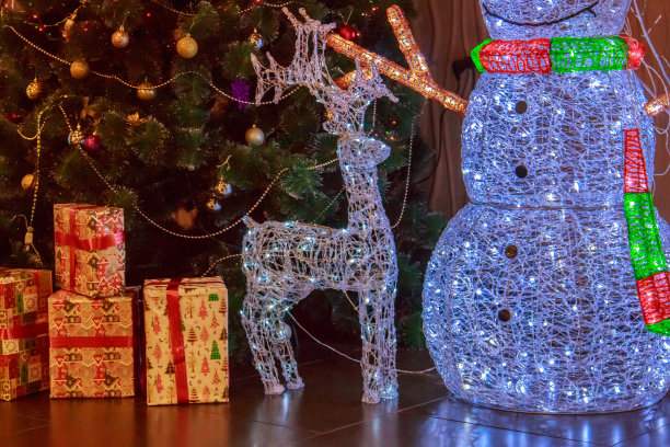 在人造圣诞树的背景上，有一个大的新年人物雪人，一只鹿和发光的五彩花环图片下载
