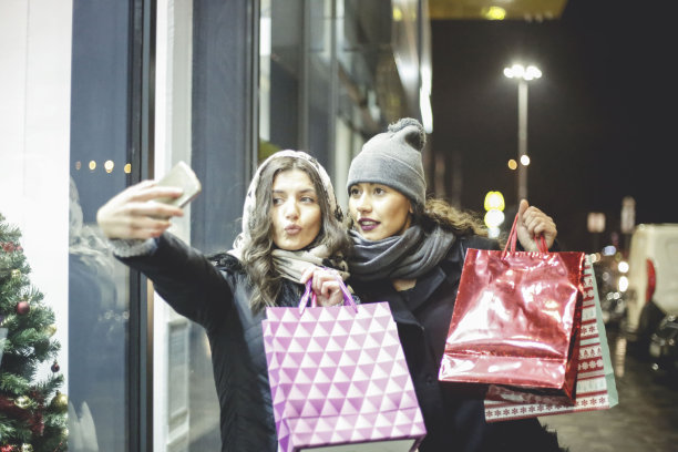 两个女性朋友一起购物，她们利用这个机会用智能手机自拍图片下载