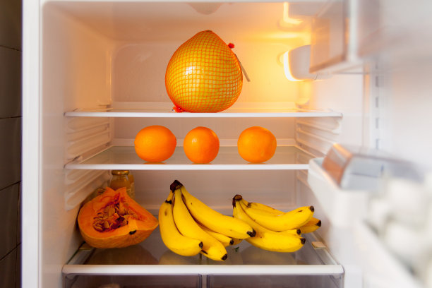 打开冰箱，白色的架子上放着橙色和黄色的水果。健康饮食的概念。图片下载