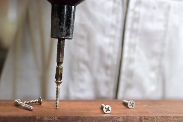 在木工车间，用白色制服的木匠的双手，用电动工具拧紧螺丝。选择性聚焦和浅景深。图片下载