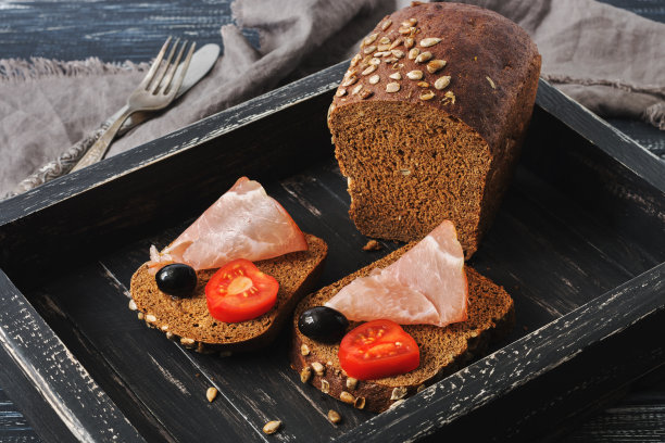 黑面包火腿，橄榄和西红柿放在黑色的木托盘上。与火腿三明治。图片下载
