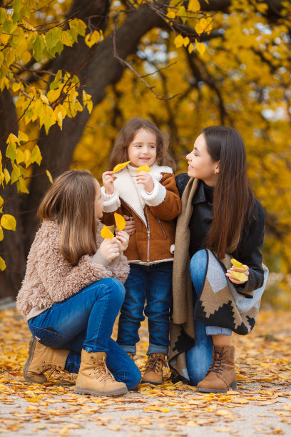 三姐妹有乐趣在秋天公园的树木与黄色和红色的树叶图片下载