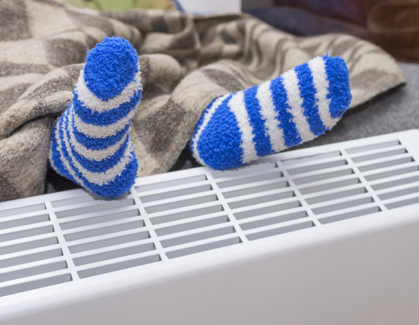 把孩子的脚放在毯子下面，用暖和的毛巾布袜子放在电热器上。家用通用电对流器。图片下载