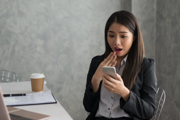 兴奋的亚洲商务女孩，而阅读智能手机坐在她的工作站。企业成功的概念图片下载