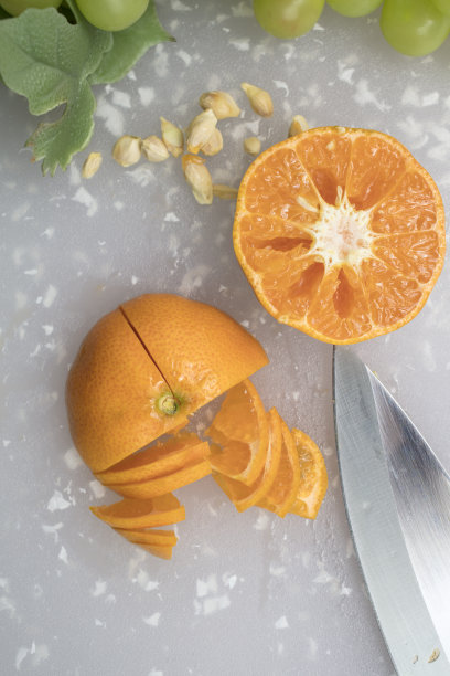 用葡萄、瓜子和刀在砧板上切橘子图片下载