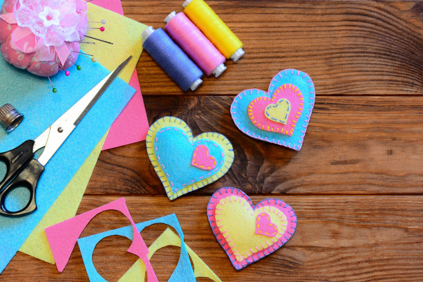 情人节饰品创意。毛毡心饰品，剪刀，线，针垫，顶针，木桌上的毛毡床单和碎片。情人节缝纫项目。情人节浪漫的礼物图片下载
