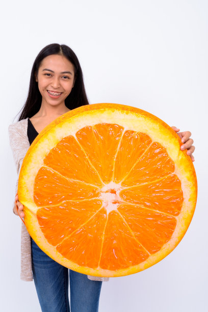 年轻亚洲妇女的肖像，站在白色背景下，拿着大橙色水果图片下载