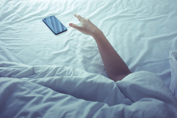 年轻女子早上睡在床上玩手机。生活方式的概念图片下载