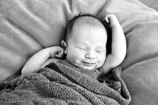睡着的男婴裹着羊毛毯子躺在垫子上——黑白相间图片下载