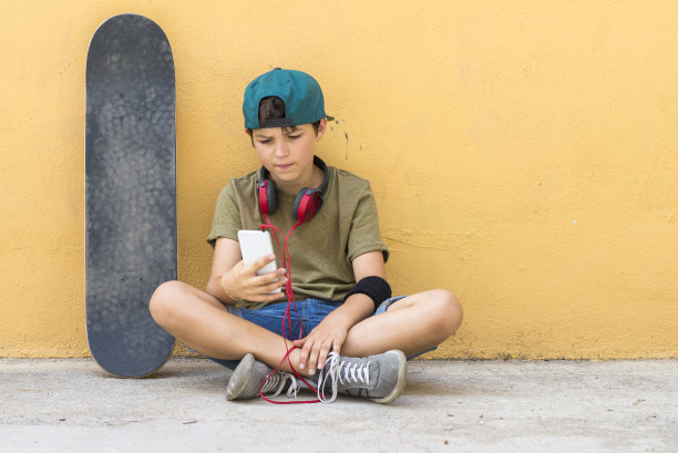 一个青少年坐在街道上聊天的肖像(滑板在墙上)图片下载