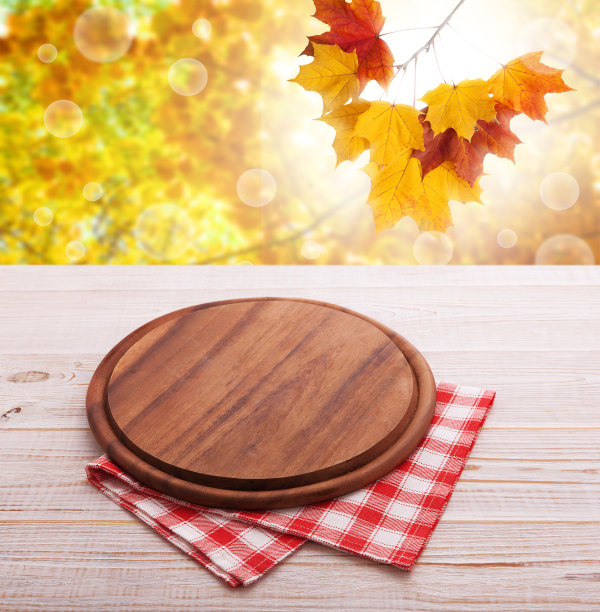 披萨板用餐巾放在木桌上，以秋叶为背景。厨房背景，产品蒙太奇展示。模拟。图片下载