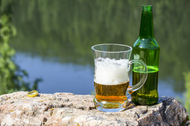 马克杯和一瓶啤酒放在河上的一块岩石上图片下载