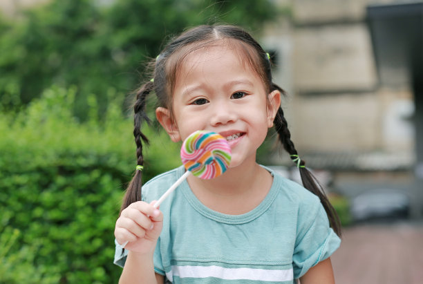 特写快乐的亚洲小女孩与棒棒糖。盯着她的脸。图片下载