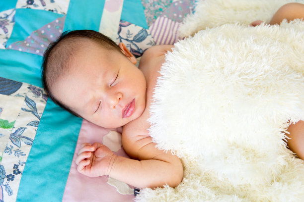 刚出生的男婴裹着蓬松的奶油毯子，睡在铺着的被子上图片下载