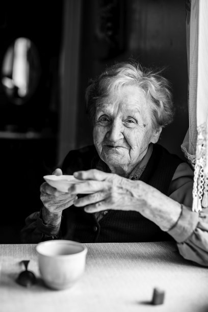 一位老妇人坐在桌旁，用茶托喝茶。黑白肖像。图片下载