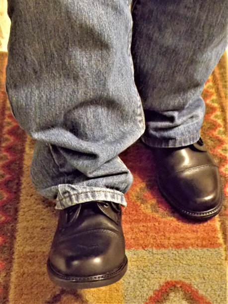 低头看着一个穿着浅蓝色牛仔裤和擦得锃亮的黑色皮鞋的男人走向摄像机图片下载