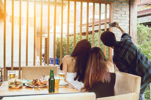 两名亚洲妇女和一名男子手持手机拍摄餐桌上的食物图片下载