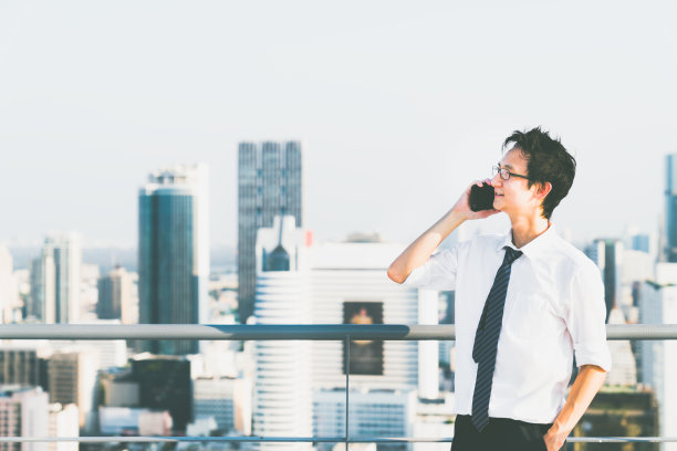 年轻的亚洲商人在建筑物屋顶上用手机打电话，在城市景观背景上复制空间。商业沟通，商业活动，电话营销，或办公室工作人员的生活方式概念图片下载