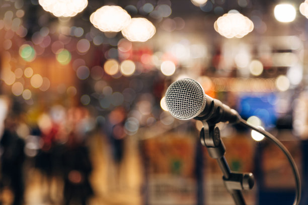 麦克风放在一个架子上，准备现场音乐表演或卡拉ok之夜，柔和的散景灯光和人们的剪影作为背景。概念为音乐演唱活动，有一个美好的时光。素材图片