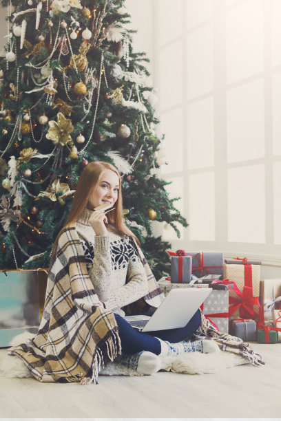 年轻女子在舒适的圣诞室内网上购物图片下载