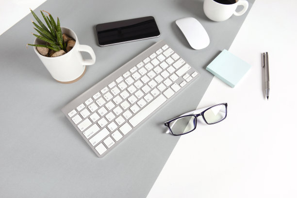 办公室桌子的平面照片，键盘，笔记本，数字平板电脑，手机，铅笔，眼镜在现代两种色调(白色和灰色)背景。桌面办公室模型概念。图片下载