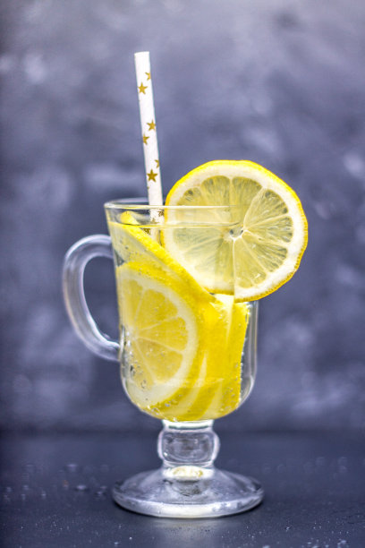 在灰色的混凝土背景下，用一个有把手的玻璃杯自制柠檬水。水和柠檬片在深色的背景。图片下载
