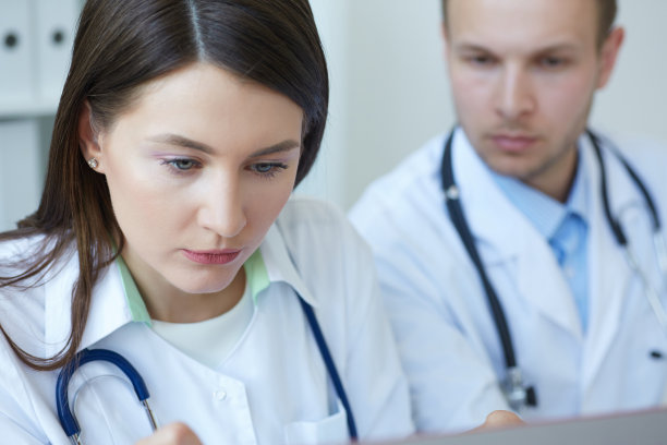 两位医生在办公室开会时一起讨论新的治疗方法的照片。医生一边使用台式电脑一边讨论新的治疗方法。图片下载