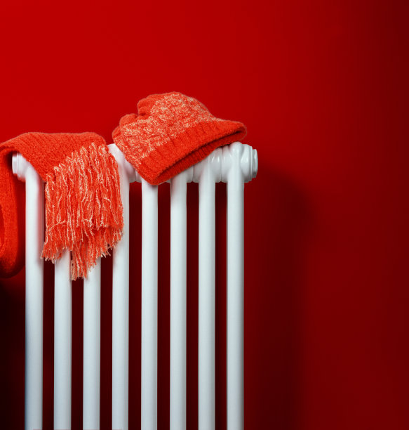 橙色针织帽和围巾躺在白色暖气片上，红墙背景图片下载