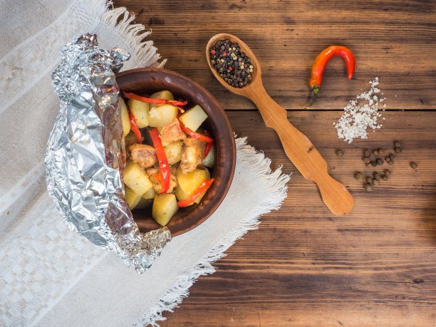 和鸡肉一起放在装有土豆的陶瓷碗里烤。以旧木头和粗糙织物为背景的乡村风格静物画。随行的木勺上放着胡椒粉和香料，俯视图图片下载