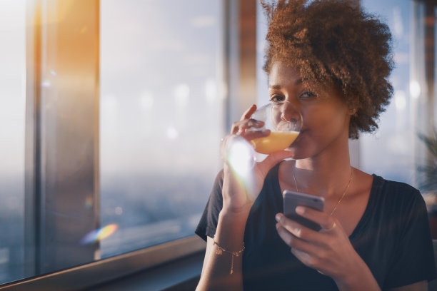 迷人的黑人女孩喝果汁，用智能手机聊天素材图片