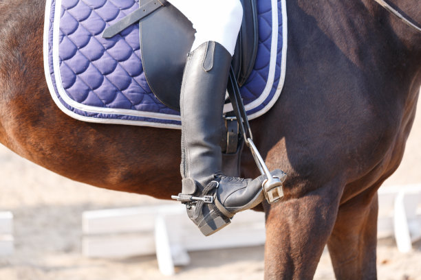 一个穿着黑色马靴的人骑着一匹黑马。在户外。素材图片