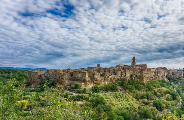 意大利托斯卡纳的皮蒂利亚诺古城的水平照片。这个城镇是用凝灰岩建造的。可以看到树林和灌木丛之间有一条通往镇上的路。天空是蓝色和多云的。图片下载