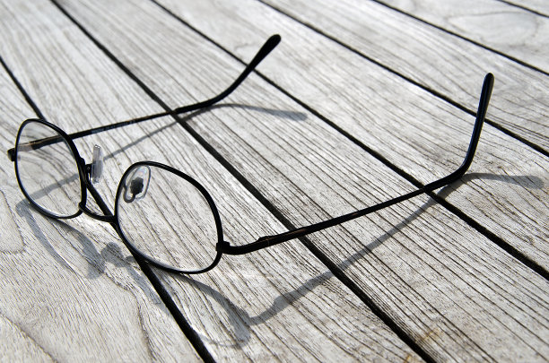椭圆形薄金属眼镜框架与清晰的镜头在木桌上。图片下载