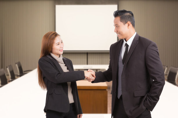 商人和女人握手在会议室背景。图片下载