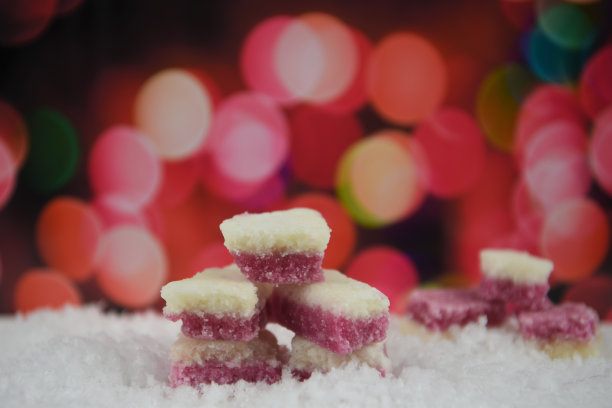 这张照片拍摄的是老式的传统英国椰子冰糖放在雪地里，背景是温馨的红粉色仙女灯图片下载