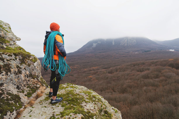 穿着羽绒服站在岩石上，肩上挎着一根绳子图片下载