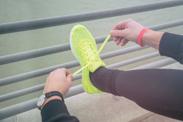 城市慢跑者在河上桥上的栅栏上系跑步鞋。图片下载