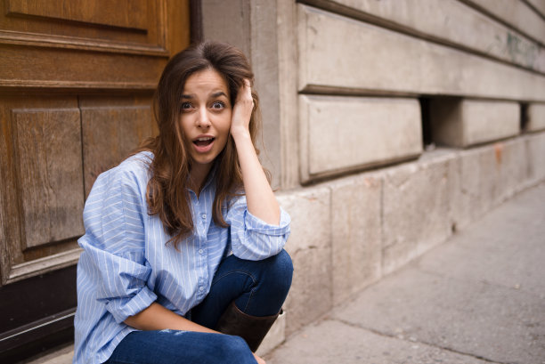 可爱的年轻女士做一个可爱的惊讶的面部表情，而坐在门前的街道在夏天。图片下载