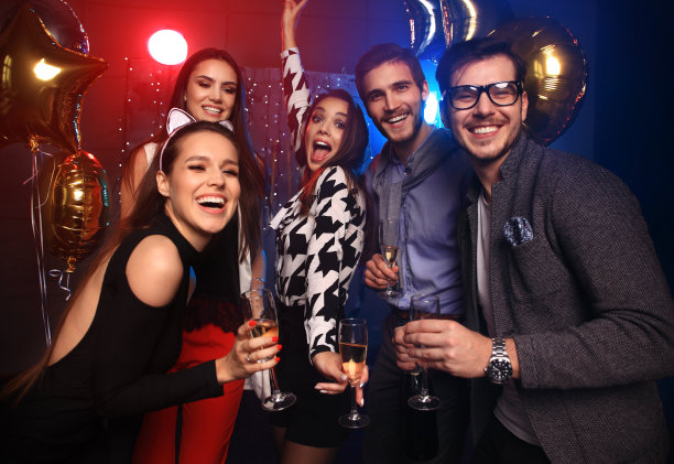 享受神奇的聚会。一群漂亮的年轻人，手拿香槟笛跳舞，看起来很开心。素材图片