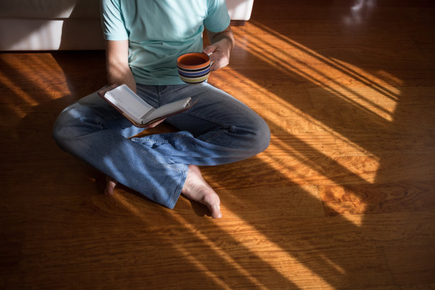 一个男人在家里棕色的地板上，手里拿着一本旧的精装书。国内的生活方式。教育的概念图片下载