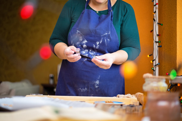 近距离照片的女人站在厨房桌子后面的家，在她的手中拿着一个饼干切割器。圣诞烘焙概念。图片下载