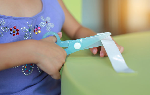 在游戏室用塑料剪刀剪纸的孩子的手。图片下载