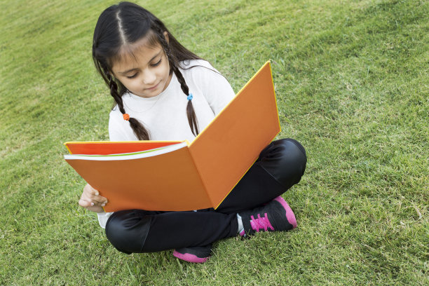 绿色的草地上，快乐的编着辫子的小女孩图片下载