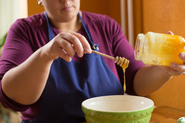 近距离照片的年轻女性拿着一罐有机蜂蜜上方的绿色碗与一只手，从罐子里得到一勺蜂蜜图片下载