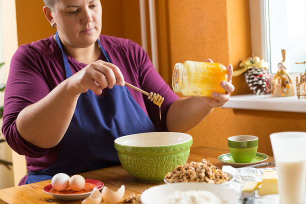 近距离照片的年轻女性拿着一罐有机蜂蜜上方的绿色碗与一只手，从罐子里得到一勺蜂蜜图片下载