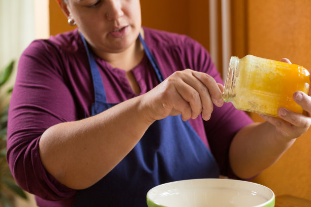 近距离照片的年轻女性拿着一罐有机蜂蜜上方的绿色碗与一只手，从罐子里得到一勺蜂蜜图片下载