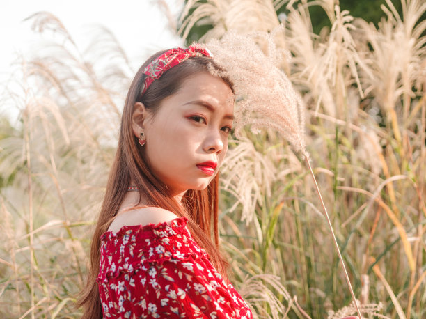 一个美丽的中国女孩的肖像站在黄色的芦苇田在阳光明媚的秋日。素材图片