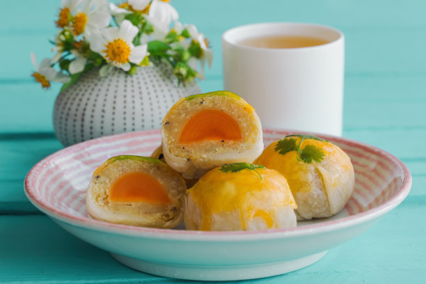 精美的中式点心或月饼夹绿豆沙和咸蛋黄在陶瓷盘子上，茶水在浅蓝色的木桌上。自制的面包店的概念。素材图片